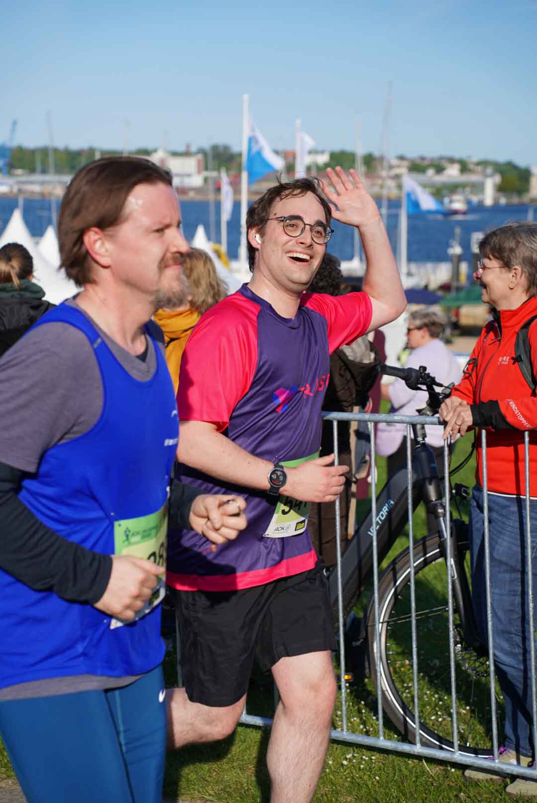 Joshua beim AOK Business Run 2025, breit grinsend und winkend beim Laufen | Joshua running at the AOK Business Run 2025, smiling broadly and waving