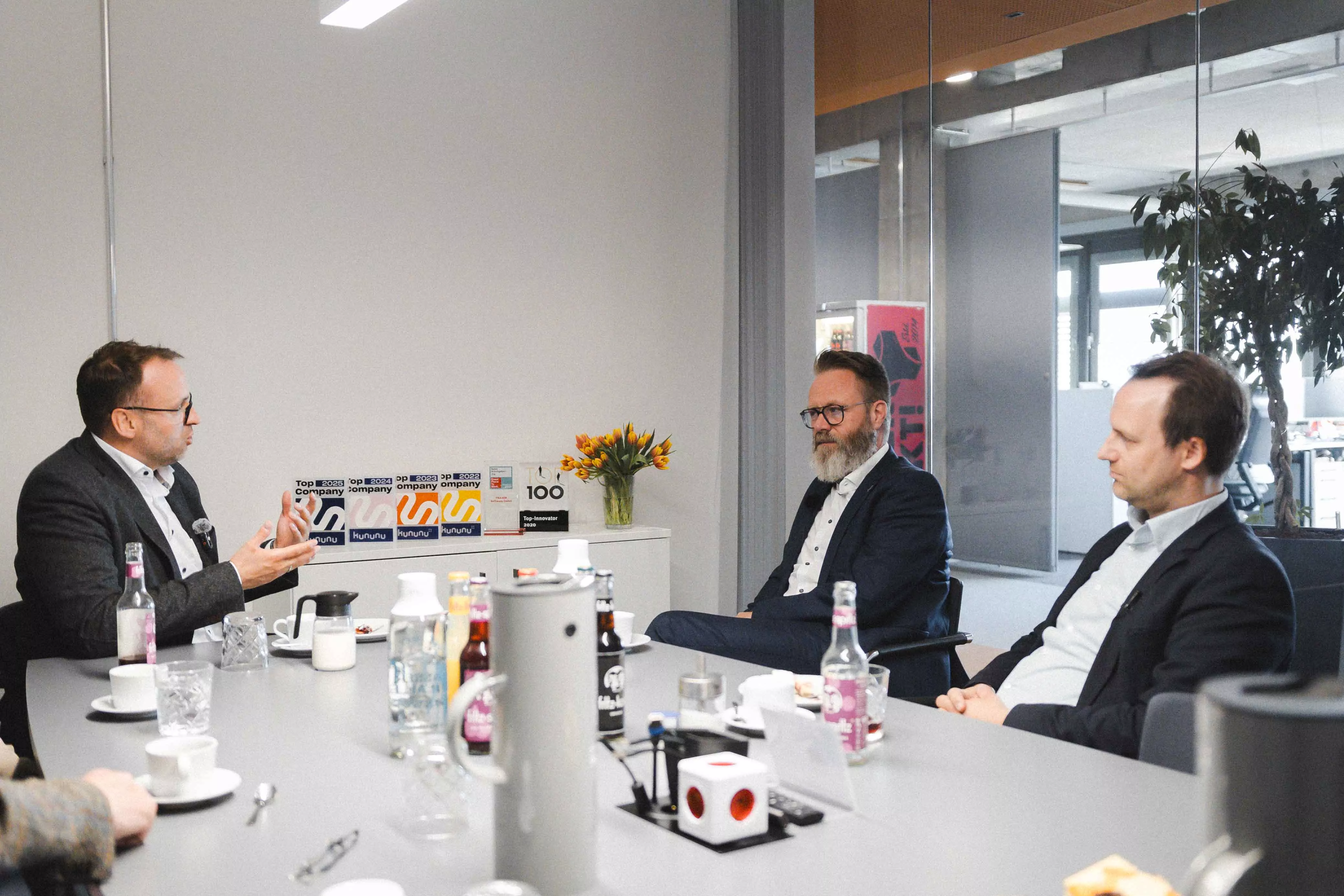 Hauke Lamb erklärt gestikulierend etwas im Konferenzraum, während Claus Ruhe Madsen und Johannes Ripken aufmerksam zuhören. | Hauke Lamb gesturing while explaining something in the conference room, as Claus Ruhe Madsen and Johannes Ripken listen attentively.