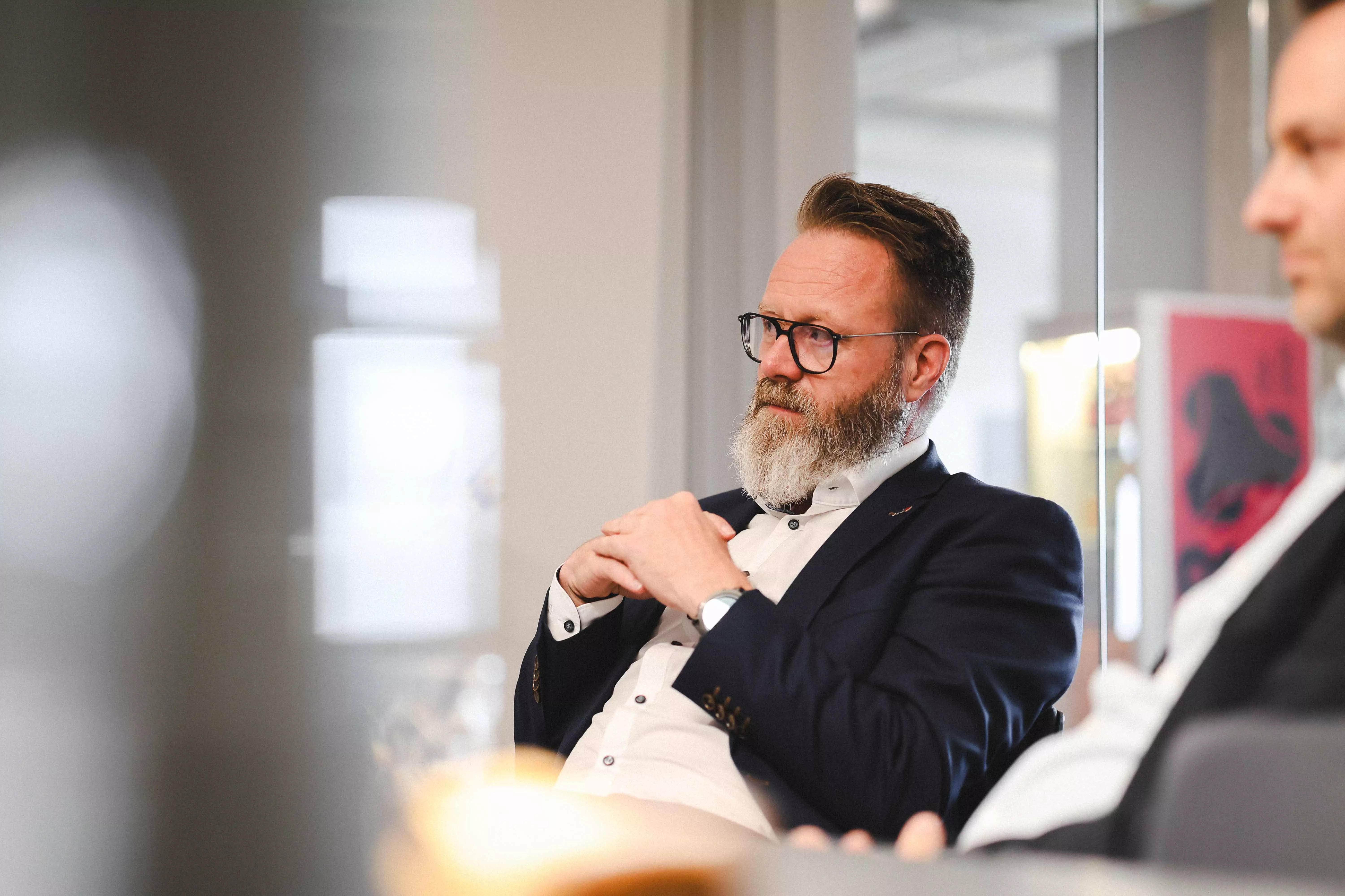 Claus Ruhe Madsen hört aufmerksam zu und hat die Hände ineinander verschränkt. | Claus Ruhe Madsen listening attentively with his hands folded.