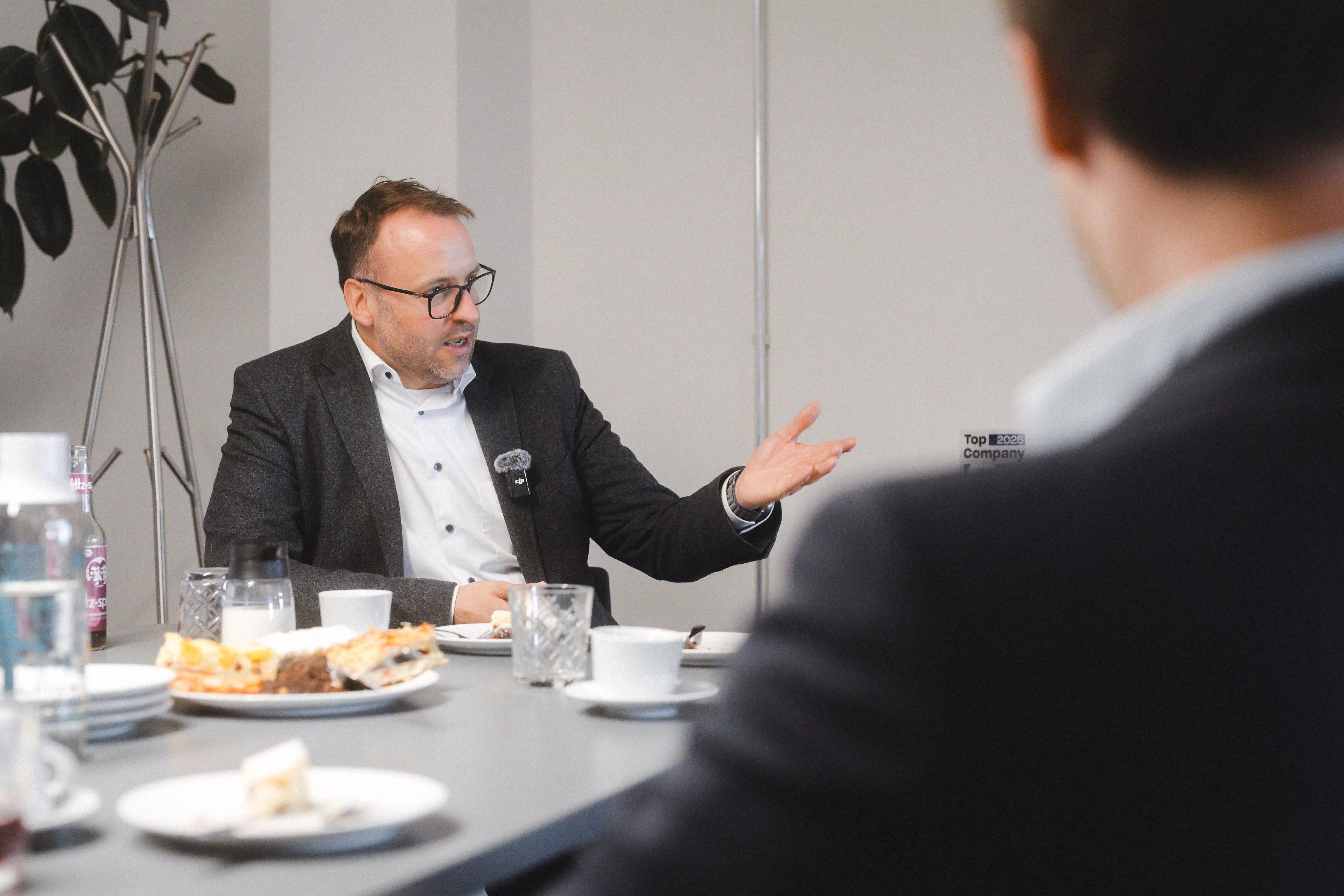 Hauke Lamb sitzt links im Bild und gestikuliert, während er etwas erklärt. | Hauke Lamb is seated on the left side of the image, gesturing as he explains something.