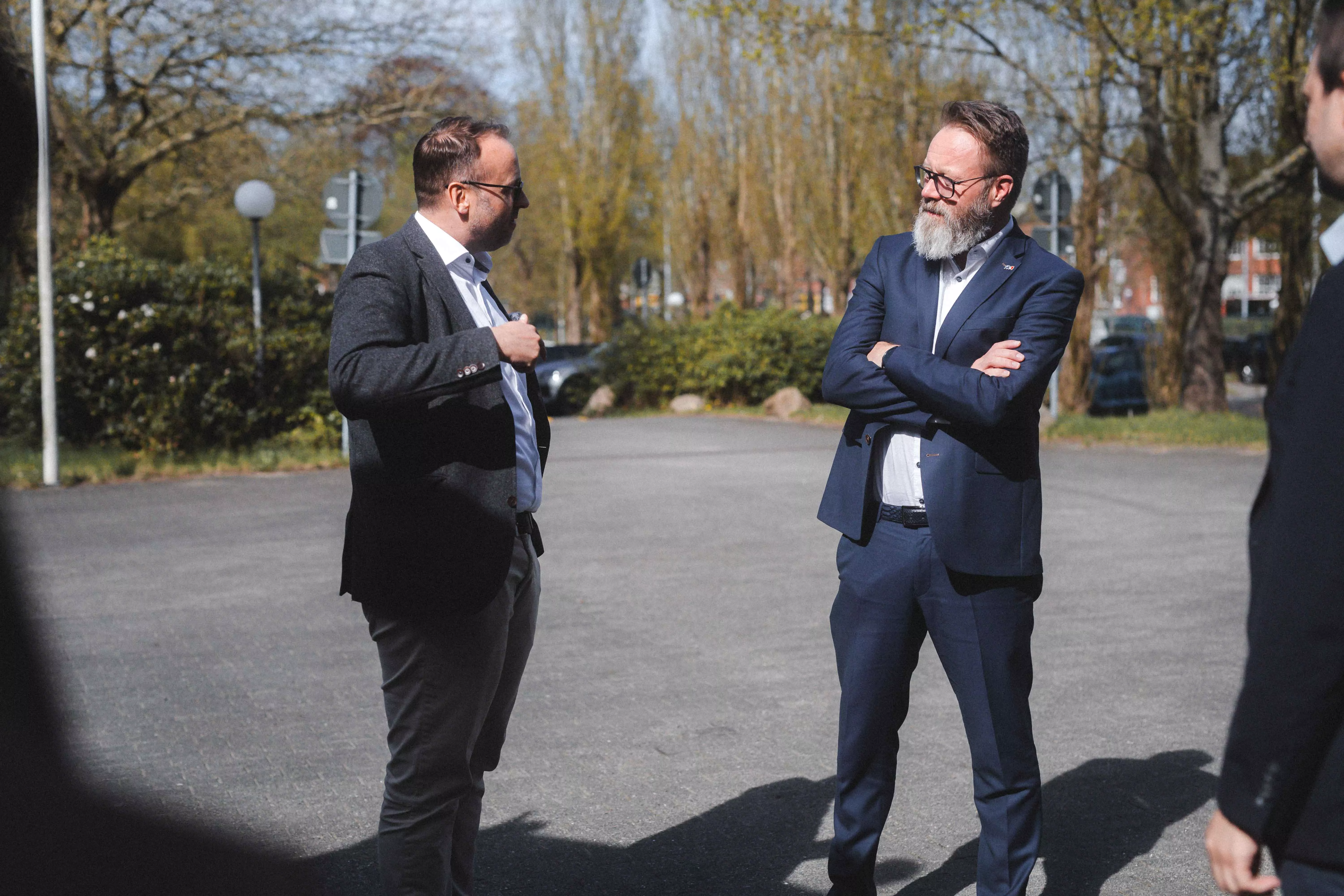 Hauke Lamb erklärt etwas und gestikuliert, Claus Ruhe Madsen steht mit verschränkten Armen daneben und hört aufmerksam zu; beide stehen draußen vor einem CLAAS-Traktor, der im Bild nicht zu sehen ist. | Hauke Lamb explaining something while gesturing; Claus Ruhe Madsen stands next to him with arms crossed, listening attentively. Both are outside in front of a CLAAS tractor, which is not visible in the image.